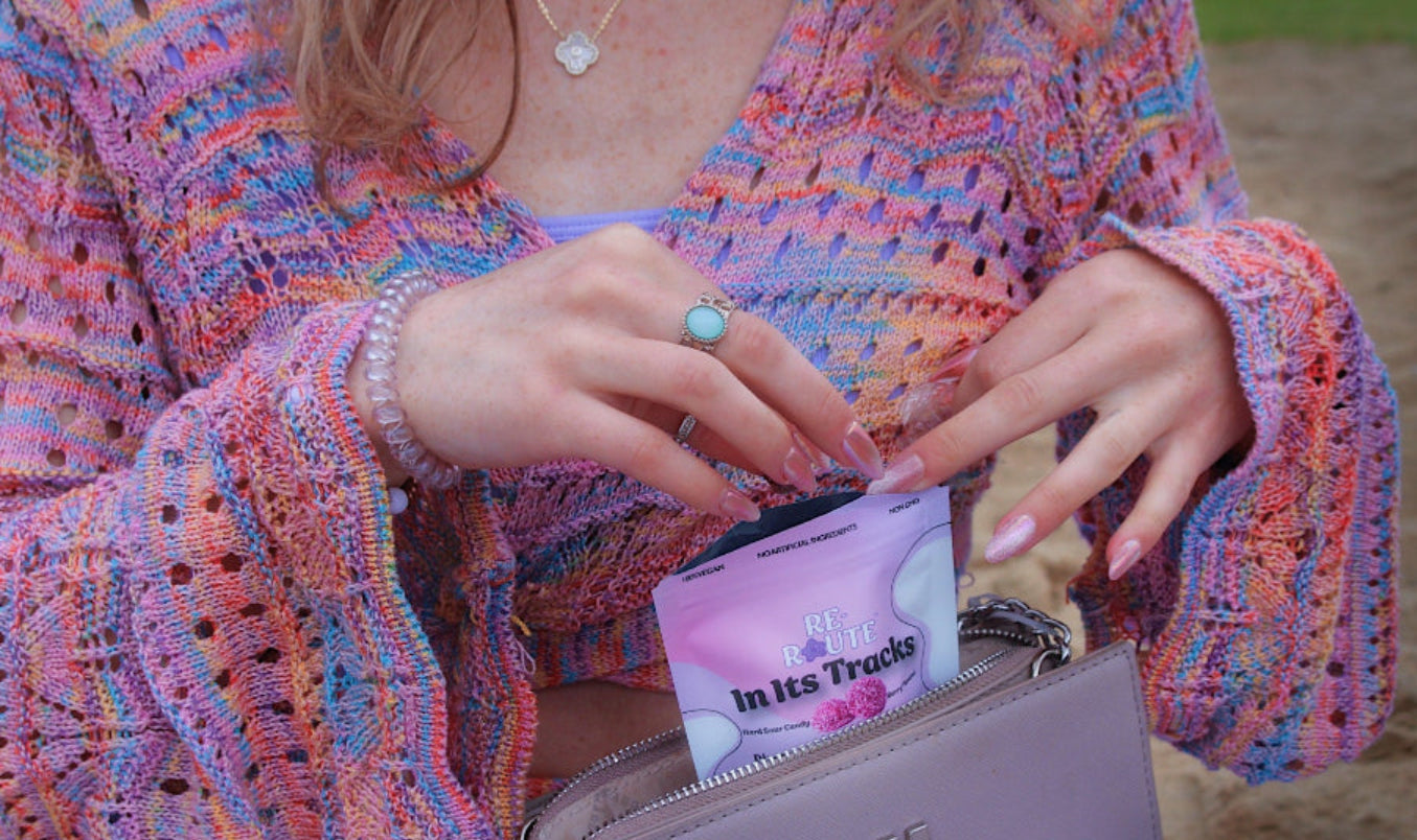 Person wearing a colorful sweater with a pink pouch containing a product labeled 'In Its Tracks', an all-natural hard sour candy with adaptogens and vitamin D. How to calm myself from anxiety