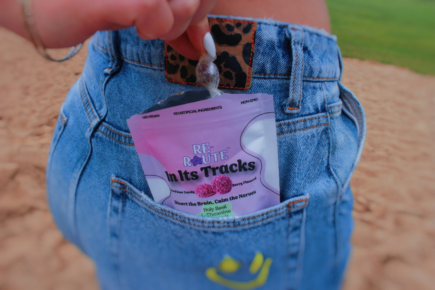 Person wearing blue jeans with a pink package labeled 'In Its Tracks' in the pocket. Organic hard sour candy supplement. Vitamins for panic attacks support.